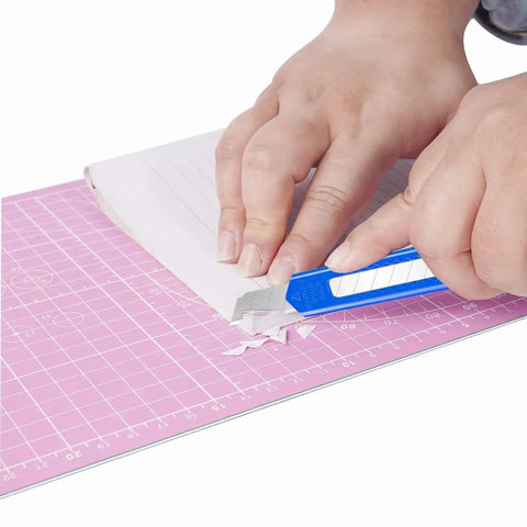 Person using blue 8 Pack 9mm Wide Box Cutters Retractable Utility Knives for Office and Craft on pink cutting mat with paper
