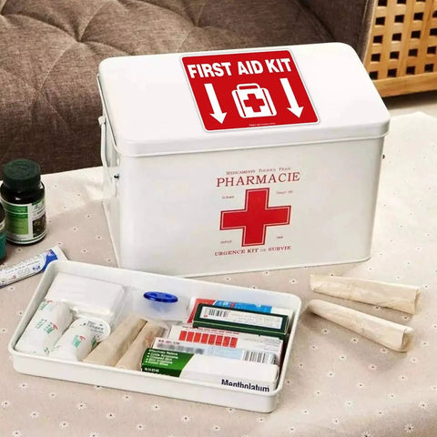 First Aid Kit with red sticker decal on lid, white box on table, various medical supplies visible inside; for quick access in emergencies.
