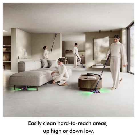 Dyson PencilVac cordless vacuum in dark gray with blue accents cleaning a modern living room; green floor lights visible.