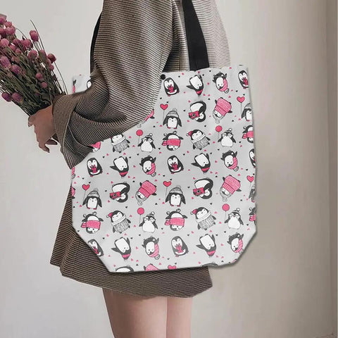 Person holding a tote bag with penguin and heart design.