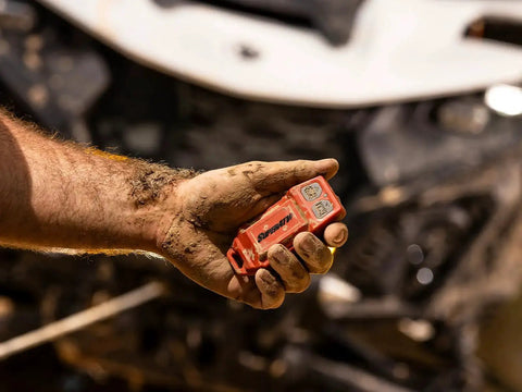 Close-up of red SuperATV winch remote control held by muddy hand