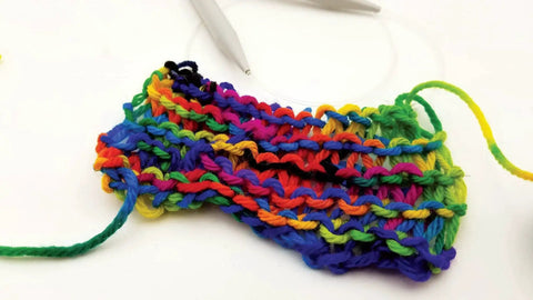 Close-up of a multicolored knitted swatch using rainbow yarn with knitting needles on a white background.