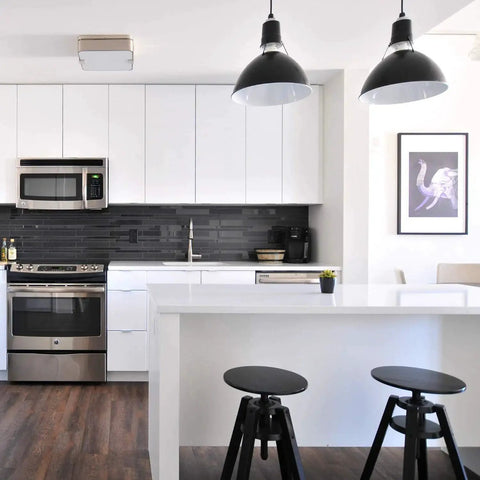 Modern kitchen with white cabinets, black backsplash, and hanging lights over a white island with black stools