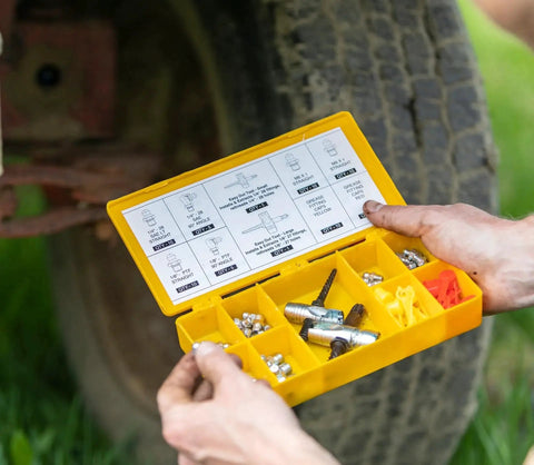 Person holding a yellow box with a grease fitting multi tool for easy install and extraction, LockNLube compatible, near a tire