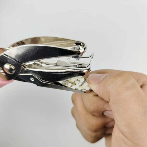 Handheld Circle Hole Punch One Ninth Inch Three Mm used to punch paper, easy grip, single hole paper punch shown in action with punched paper dots.