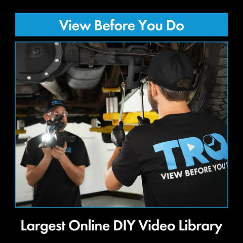 Two mechanics working on car suspension, wearing black TRQ shirts, in an automotive repair shop.