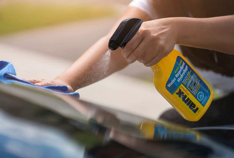 Person applying Water Repellent Glass Treatment For Rainy Day Driving That Boosts Visibility By Making Rain Bead Up And Slide Off The Windshield 473mL Bottle Rain X Original Glass Treatment on car.