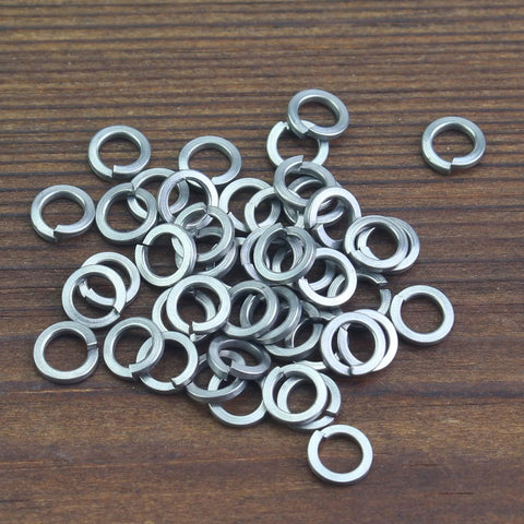 M3 stainless steel split lock washers for screws and bolts, silver, scattered on a wooden surface.
