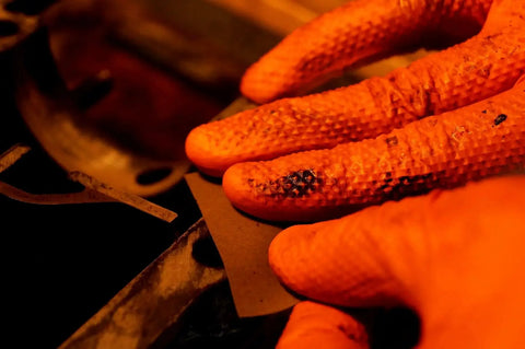 Close-up of hands wearing 8 Mil Orange Nitrile Gloves With Diamond Textured Grip For Industrial And Food, working on machinery.