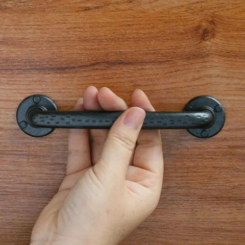 Hand holding Rustic Antique Black Cabinet Pulls Curved Zinc Alloy 5.5 Inch Length with 5 Inch Hole Center mounted on wood.