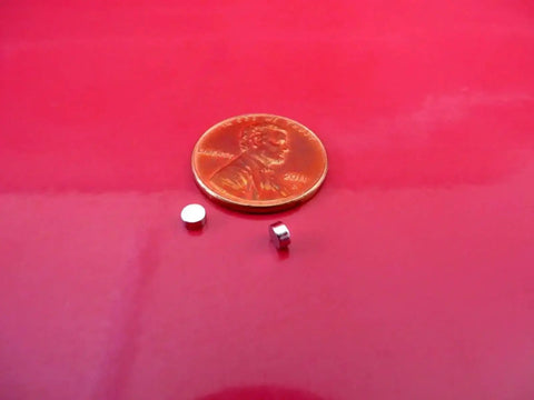 Tiny 3x1.5mm Neodymium Disc Magnets Pack Of 300 For Warhammer And Miniatures next to a penny on red background.