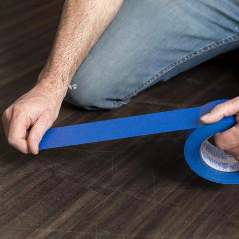 Person applying Clean Release Blue Painter's Tape 0.94 Inch Wide 60 Yards For Sharp Lines on wooden floor.