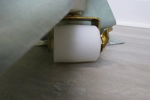Side view of 2-1/8-Inch White Bed Rollers With Side Brake, 2-Pack For Furniture Moving, installed on a bed frame, on a wooden floor.