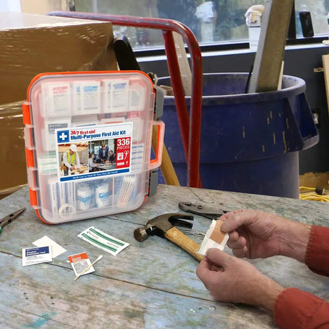 All-Purpose 100-Person Emergency First Aid Kit For Office, Home, And Car with open case showing supplies on a workbench