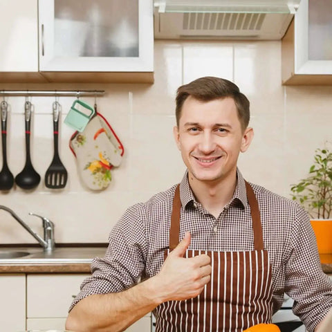 Person in striped apron smiling in kitchen with modern utensils and vegetables, showing approval with a thumbs up.