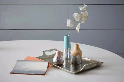 Metal leafing on ceramic vases on a tray with silver sheets, using Mona Lisa Water Based Sealer For Metal Leafing Projects By Speedball.