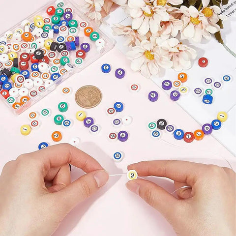 Hands arranging 200 Piece Billiard Ball Print Polymer Clay Beads Set for DIY Jewelry Making, colorful flat round spacer beads on a table.
