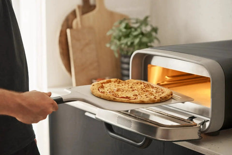 Compact 12 Inch Aluminum Pizza Peel with Handy Handle turning a pizza in an outdoor oven. Lightweight, durable design.