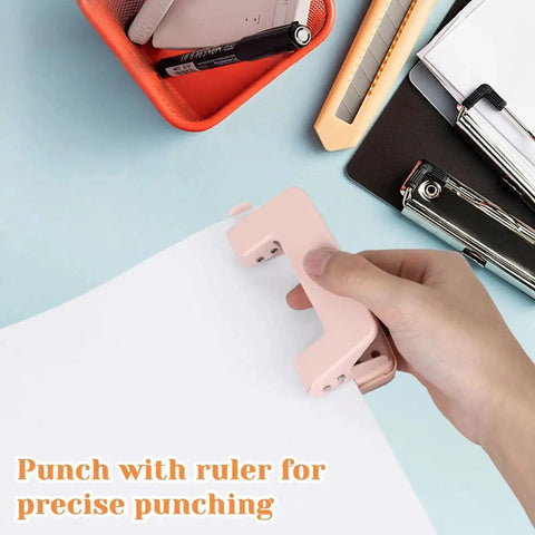 Hand using pink two-hole punch with ruler on paper for precise punching; compact metal tool for A4 A5 B5 sheets, low force, up to 10 sheets.