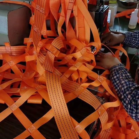 Person assembling Flat Nylon Sling Hoisting Net For Heavy Load Rigging With 10cm Mesh, showcasing orange high-tenacity polyester.