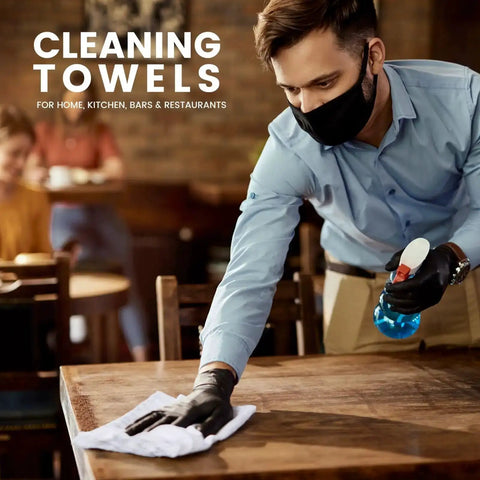 Man cleaning a wooden table with white towel from Absorbent Quick Dry Bar Mop Towels Pack Of 60, 14x17 Commercial Grade Cotton Cleaning Rags For Kitchen And Bar, White Reusable Shop Towels For Heavy Duty Cleaning And Spill Cleanup, wearing gloves and mask in a restaurant setting.