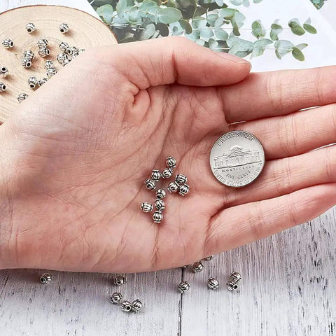 Hand holding Antique Silver Tibetan Style Pumpkin Spacer Beads 4mm, 100 Piece Set with a coin for size reference.