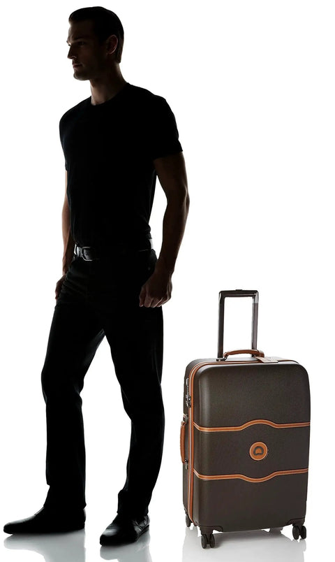 Man standing with Chatelet Hard Plus Hardside Luggage With Spinner Wheels In Chocolate Brown For Checked Medium 24 Inch Travel by Delsey Paris