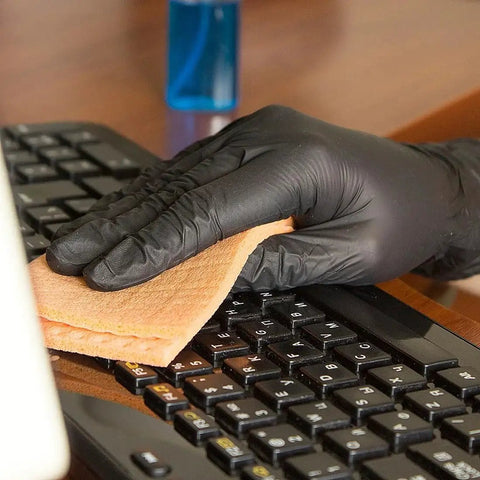 Hand in Black Nitrile Gloves 4 Mil Large 100 Count Chemical Resistant Food Safe wiping a computer keyboard with a cloth.