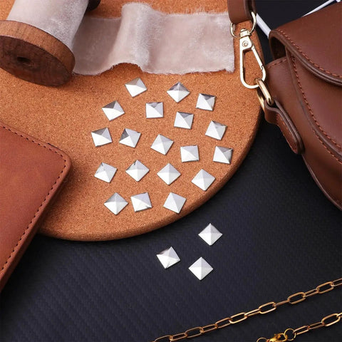 Silver Pyramid Spike Flatback Studs 200Pcs For Clothing Belts Leathercraft displayed on a surface with leathercraft tools.