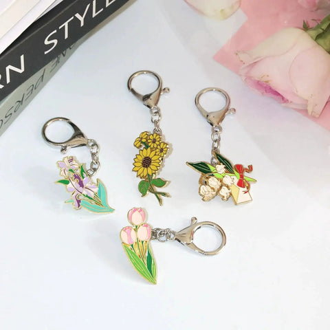 Colorful enamel pin keychains with floral designs, featuring 6 Pack Pin To Keychain Converter Locking Backs Turn Pins Into Keychains For Display On Bags And Accessories Enamel Pin Backing Brooch Holder Durable Metal Construction For Everyday Style And Easy Show Off, arranged on a white surface.