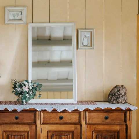 Wooden dresser with decorative mirror and floral arrangement on wall
