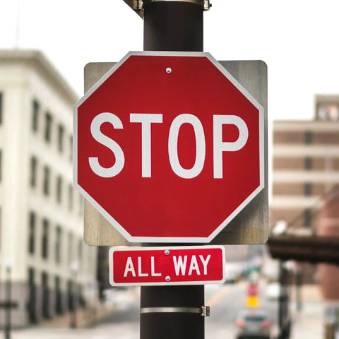Red octagonal stop sign with a smaller rectangular 'All Way' sign below it on a metal pole, blurred urban background.
