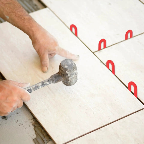 Person installing tiles using Color Coded Plastic Horseshoe Shims For Leveling Tiles And Windows 600 Pieces, visible in red.