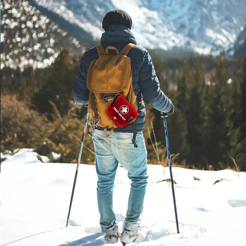 Person hiking in snowy mountains with a red Mini First Aid Kit For Home Car Travel And Outdoor Adventures 137 Piece Emergency Medical Kit
