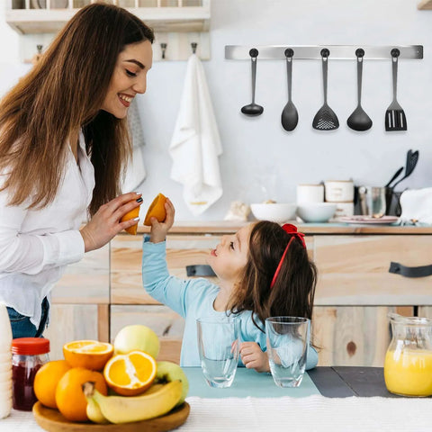 Mother and daughter in modern kitchen with fruit on table, smiling and preparing food, utensils hanging on wall, warm family moment.