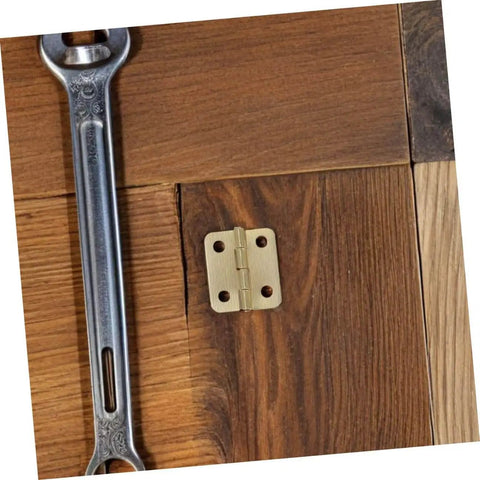 Close-up of a gold miniature iron hinge installed on a wooden surface next to a wrench, part of a 40Pcs Miniature Iron Cabinet Hinges kit.