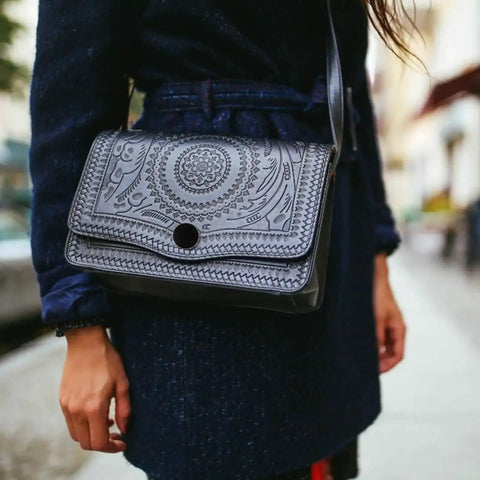 Woman carrying a black embossed leather shoulder bag on the street, wearing a navy coat.