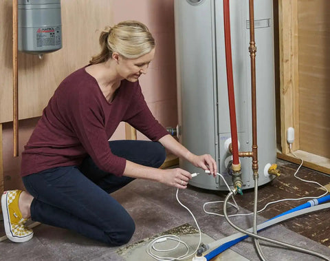 Woman installing Smart WiFi Water Leak Sensor With Freeze Detector And Humidity Monitoring For Home Leak Alarm near water heater