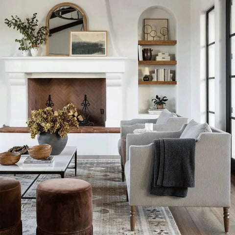 Modern living room with gray sofas, wooden shelves by fireplace, decorative vases, plants, and abstract art.
