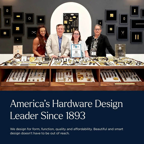 Group of people standing behind a display of various door hardware and handles in a showroom setting.