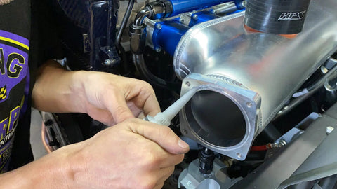 Permatex Ultra Grey RTV silicone gasket maker being applied to a metal engine intake flange.
