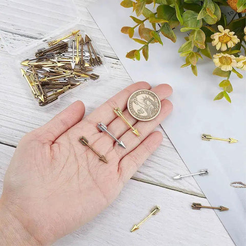 Hand holding Arrowhead Charms 60Pcs Set in gold, silver, bronze with coin for size comparison, showcasing three color Tibetan style alloy charms.