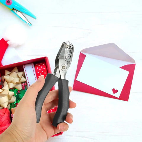 Hand holding Metal Single Hole Puncher With Ergonomic Handles And Built In Guide For Home Office Crafts, over craft supplies