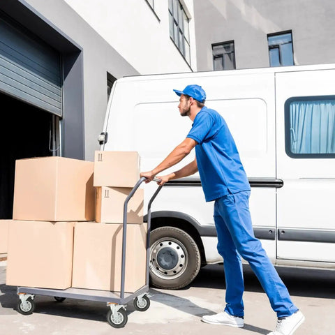 Person in blue uniform pushing a cart with boxes near a delivery van outside a warehouse
