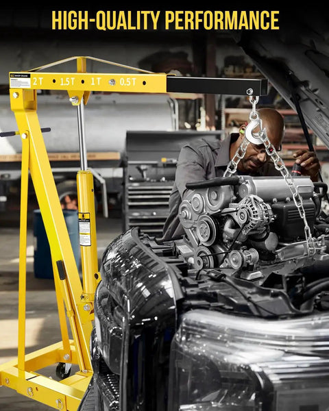 Yellow hydraulic 2-ton shop crane with folding arms and 6 steel casters lifting a car engine in a workshop