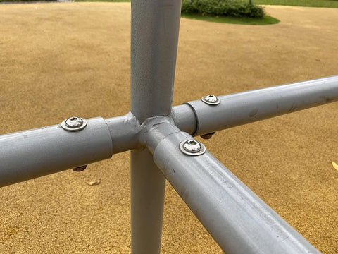 Stainless steel flat washers on a gray metal pipe cross joint, outdoor setting, close-up.