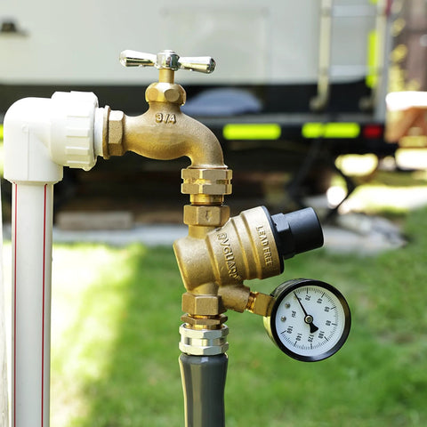 Front view of brass RV water pressure regulator valve with gauge and inlet screen filter connected to a white pipe fitting