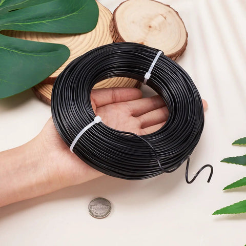 Black Aluminum Craft Wire 180 Feet 12 Gauge Bendable Wire For DIY Beading Jewelry Making held in hand with coin for scale.