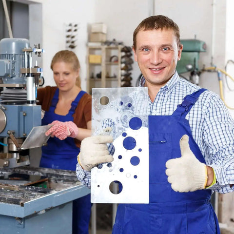 Factory worker holding metal sheet with drilled holes, machine in background