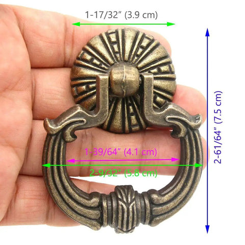 Close-up of a vintage brass ring pull handle with dragon head motifs, hand-held, showing detailed engravings and pumpkin style disk base.